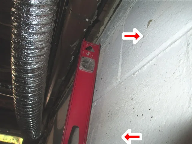 Level held against a cracked block basement wall, with red arrows marking the crack
